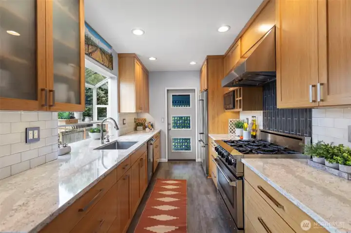 A well-designed kitchen with a commercial-grade six-burner gas range, custom cabinetry with generous storage, and a garden window above the sink that fills the space with light and greenery. A well-designed kitchen with a commercial-grade six-burner gas range, custom cabinetry with generous storage, and a garden window above the sink that fills the space with light and greenery.