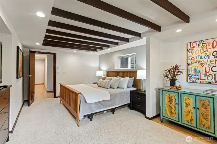Spacious and well-appointed, the lower-level primary features dark stained ceiling beams, recessed lighting, and plush carpeting. Private and quiet. A custom walk-in closet is just steps away. Spacious and well-appointed, the lower-level primary features dark stained ceiling beams, recessed lighting, and plush carpeting. Private and quiet. A custom walk-in closet is just steps away.