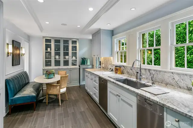 With a full wall of divided-light windows ushering in garden green, the Kitchen balances precision and polish. Waterfall-edge marble countertops and a custom glass hutch underscore both function and beauty—an inviting space where mornings begin with light and leisure.