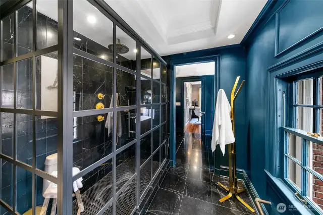 Drenched in peacock blue and lit like a stage set, the En Suite Bath/Dressing Room delivers high drama with polished black marble, steel-framed shower doors, and brass accents. Equal parts boudoir and spa, it transforms the daily routine into an immersive experience.