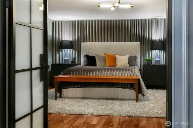 Behind steel-framed doors, the Club Room/Suite 5 evokes penthouse chic with a textural stripe wallcovering, floating nightstands, and sculptural lighting. Designed as a sybaritic guest retreat or private quarters, this space brings luxe hospitality to the garden level.