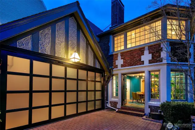 Evening falls on the Auto Court, where the original Tudor silhouette meets modern lines. The trackless glass-paneled garage door hints at the space’s dual life as both Garage and Home Gym, while soft interior glow and leaded glass windows welcome you back to a home of layered elegance.