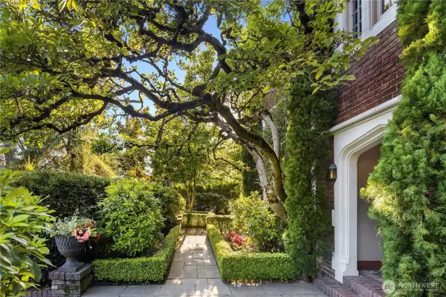 The path to the Main Gate unfolds beneath the sweeping branches of a heritage oak—one of many layered elements in the home’s tapestry of landscape and legacy. With clipped boxwood, ivy-clad brick, and dappled sunlight, this garden passageway feels both stately and alive.