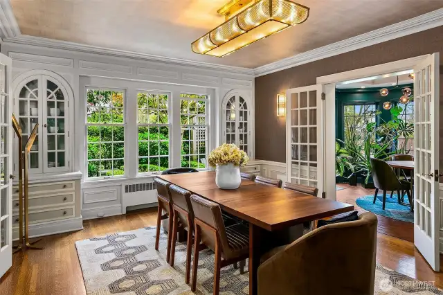 A luminous Dining Room where elegance lingers in every detail—from arched built-ins to finely cased windows framing the garden beyond. Grasscloth walls and a sculptural mid-century fixture bring softness and sheen, while French doors open to the vibrant Solarium, offering seamless flow for dinner parties and daylight reverie.