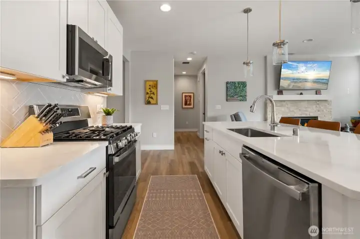 Kitchen to Great Room Flow – Sleek quartz island with sink and pendant lighting opens to the living area with cozy fireplace, creating the perfect space for cooking, dining, and entertaining.