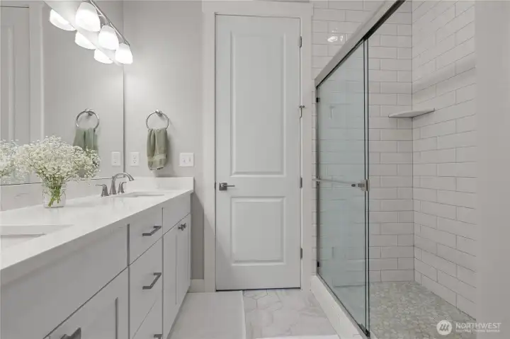 Primary Bath Shower View – Modern walk-in shower with subway tile surround and frameless glass doors complements the dual-sink vanity and quartz counters.
