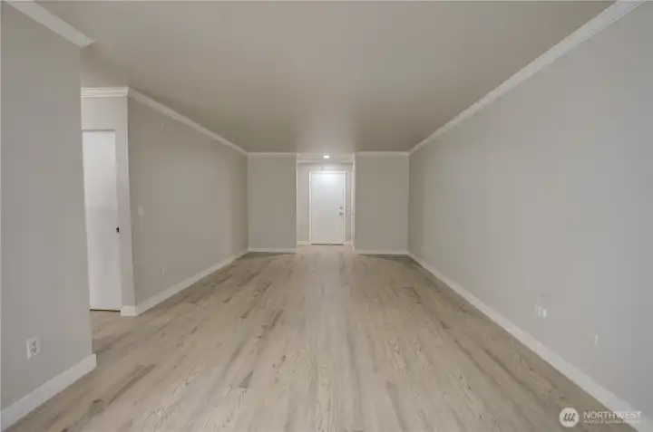 Long open layout for living and dining space - looking to the unit door. Hallway to the left in middle of room. Brand new light colored LVP flooring and freshly painted walls in a neutral tone bring a brightened look to the space. Recessed light installed throughout the ceiling for a clean look.