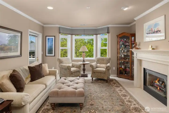Generous living room features gas fireplace, bay windows, lighting upgrades, crown moulding, and access to deck with verdant city and territorial views.