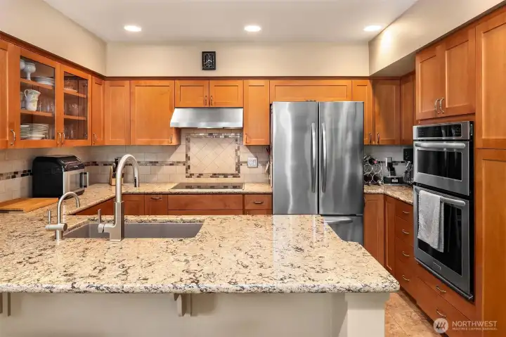 Cohesive kitchen renovation features Shaker maple cabinets with display fronts, tile flooring, slab counters, upgraded lighting, stainless undermount trough sink, instant hot water, stainless appliances including induction stovetop and armoire fridge.