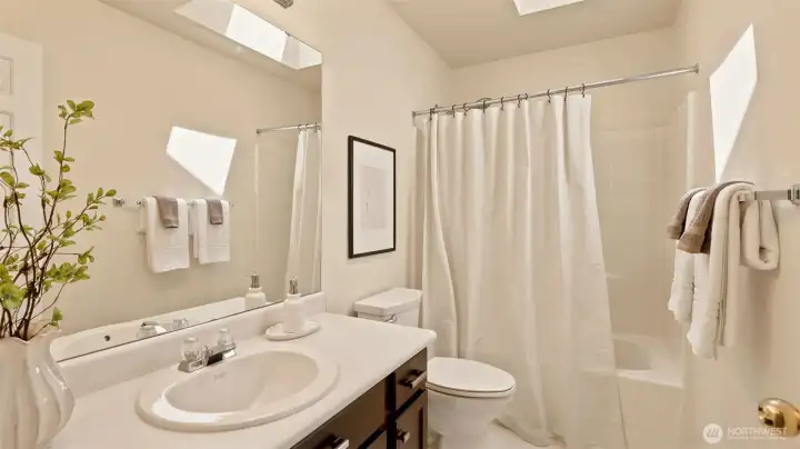 A bright and functional full bathroom featuring crisp white finishes, a large vanity mirror, and plenty of natural light from the skylight A bright and functional full bathroom featuring crisp white finishes, a large vanity mirror, and plenty of natural light from the skylight