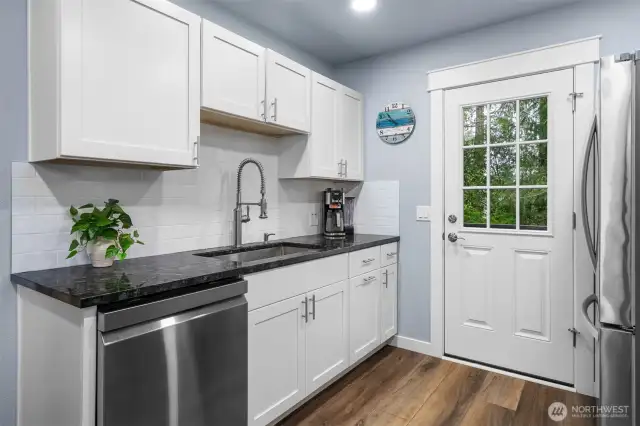 Undermount sink with modern gooseneck faucet. Doorway leads out to back deck in fenced yard.