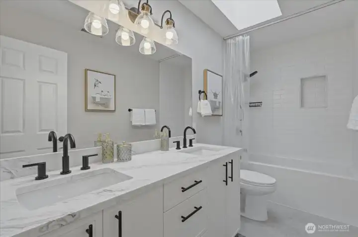 Remodled upper level bathroom with double sinks, quartz counters, custom cabinetry, a deep soaking tub and tile shower with a skylight overhead.