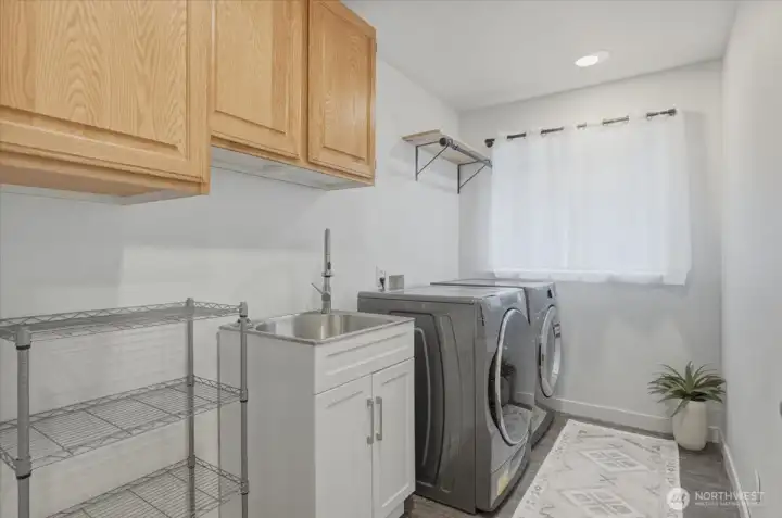 A fully equipped secondary laundry room on the lower level with side-by-side washer and dryer, utility sink and drying rack.