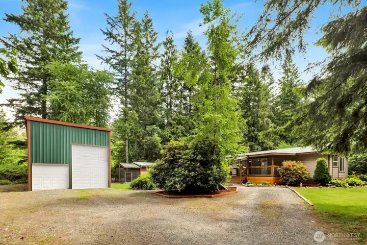 Home and detached shop surrounded by mature evergreens, established landscaping, and apeaceful setting. Virtually modified image depicting the planned large overhead door. Seller intends toinstall the large overhead door prior to closing. Actual appearance may vary until installation is completed.