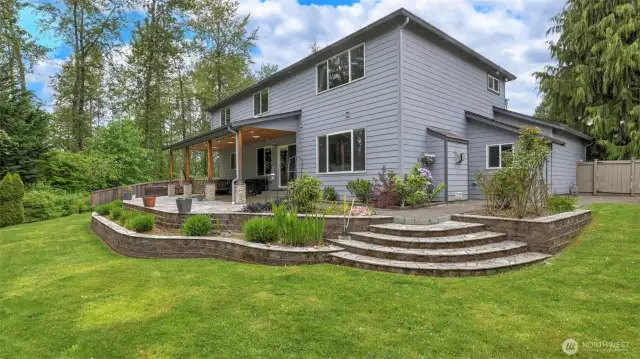 Experience outdoor living on the spacious covered patio, featuring a beautiful step-down concrete area surrounded by terraced gardens and lush greenery