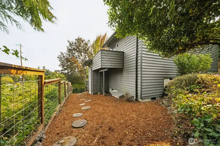 To the side of the front stairs that lead to the main entry, Is a walking path to the backyard. Note the recently installed cattle wire fencing with cedar trim. The lot is fully fenced.