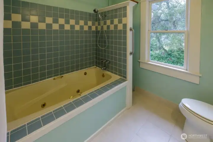 Large main bathroom with jetted tub with beautiful tile surround, pedestal sink, and cozy radiator.