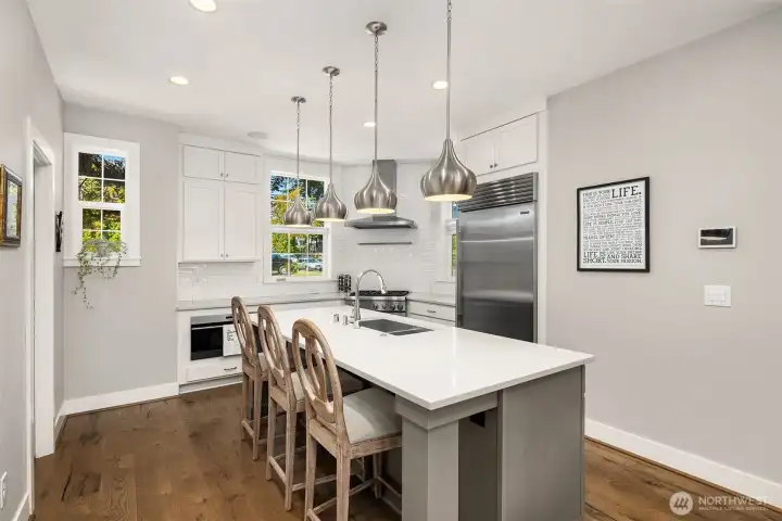 The kitchen is beautifully appointed with premium finishes, including a Sub-Zero refrigerator, granite countertops, built-in microwave, Thermador gas range, Wolf ventilation system, and a striking herringbone backsplash.