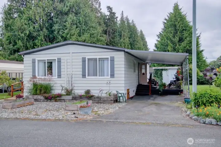West view of home with covered carport & stairs up to the large deck. Raised garden & flower beds in front of home.