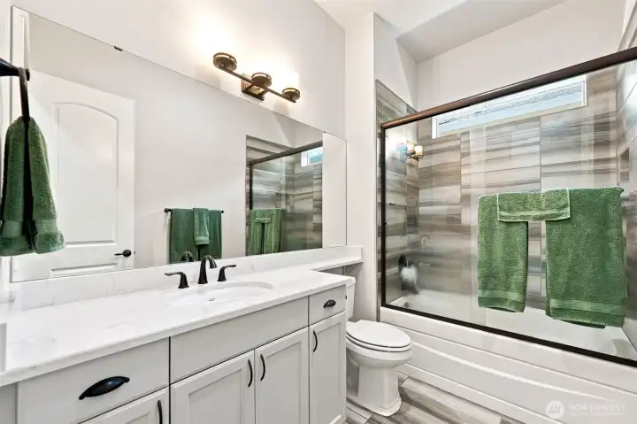 Full bathroom adjacent to bedroom #2 with quartz countertops, glass shower doors, tile surround and floors.