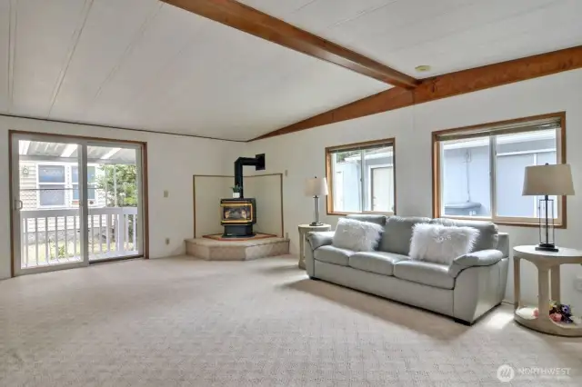 Inviting living room offers a warm and welcoming feel anchored by a free-standing fireplace nestled in the corner, perfect for cozy gatherings. Natural light pours in through a large sliding glass door which opens to a covered deck for outdoor enjoyment.