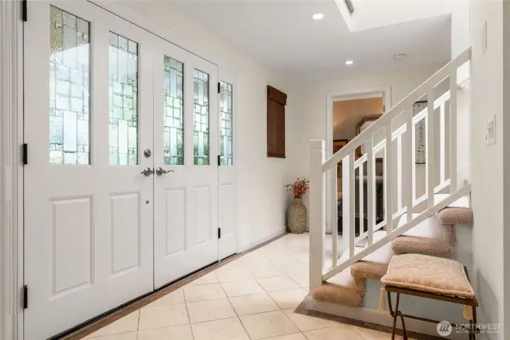At entrance, sunlight pours through the stairwell skylight, illuminating grand double doors and a striking sense of arrival