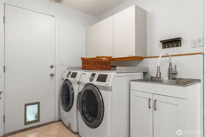 Laundry/ mud room acts as segue between kitchen and garage, equipped with built-in sink, cabinets and storage closet