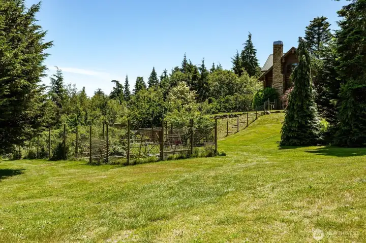 A view of the garden and fencing up to the house perched up on the hillside. A view of the garden and fencing up to the house perched up on the hillside.