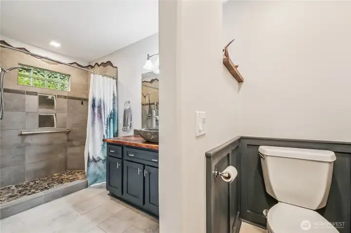 Primary bedroom bathroom features a custom shower and unique stone sink & countertop. Storage is plentiful between the storage closet and cabinet. Radiant heat flooring.