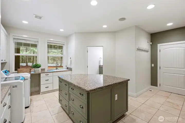 Utility room with granite-topped island for folding and extra storage, utility sink, a full bathroom, and direct access to the 3 car garage and upstairs living space.