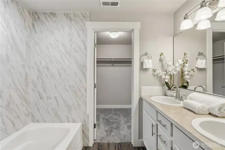 The ensuite 5-piece primary bathroom with dual sinks, floor-to-ceiling tiled surround bathtub, stand-in shower, a separate lavatory and an expansive walk-in closet.