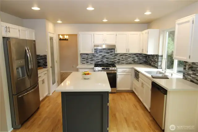 The gorgeous kitchen has white cabinetry, a tile backsplash, a spacious island, a pantry, & stainless appliances.