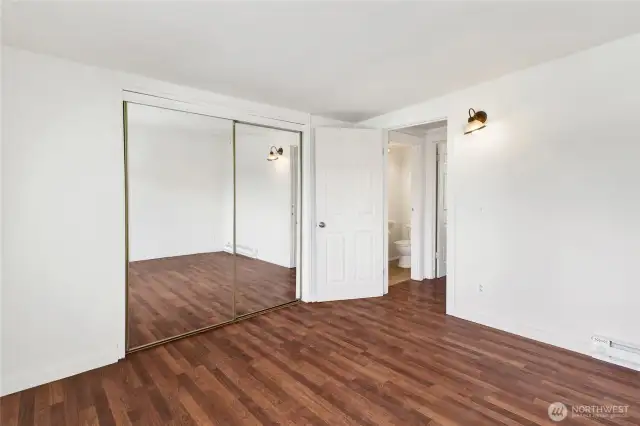 Second floor bedroom with large mirrored closet with laminate wood floors. The half bath is between the bedrooms at the top of the stairs.