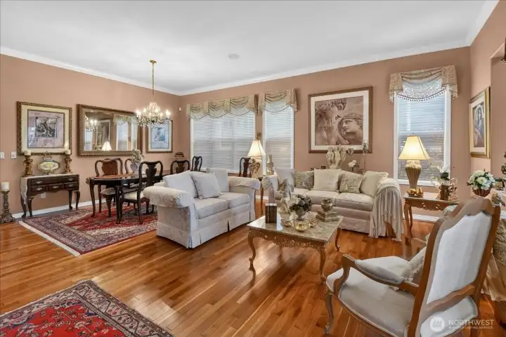 This Grand Living and Dining space is adorned with Crown Moldings, wrapped windows, elegant window treatments, a gas fireplace, classic Chandelier, and warm, custom paint.