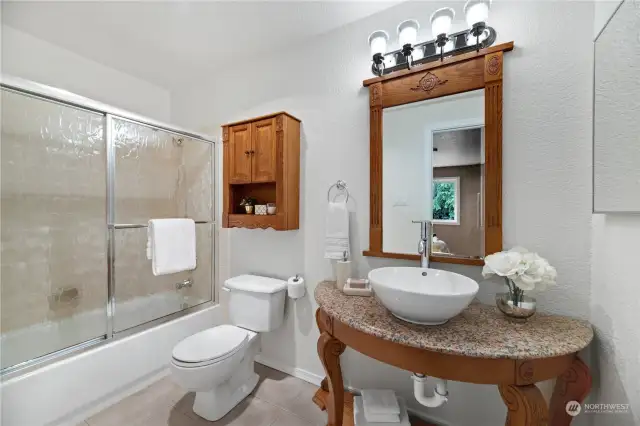 This beautifully appointed second bathroom features a stylish vanity with a vessel sink, elegant lighting, and ample storage with a custom wood cabinet. The shower-tub combo with sliding glass doors offers both convenience and a touch of luxury.