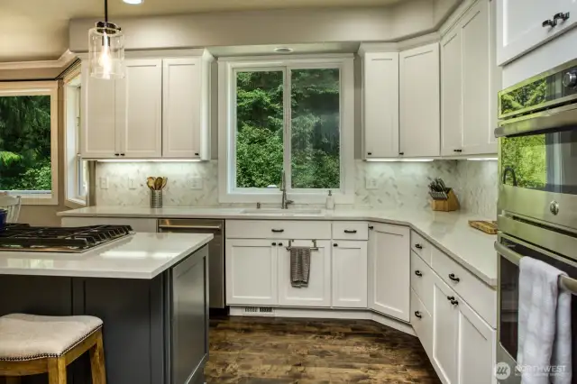 Framed by crisp white cabinetry, and hardwoods, with quartz countertops, and a classic herringbone tile backsplash in this thoughtfully designed kitchen with a fluid workflow space.