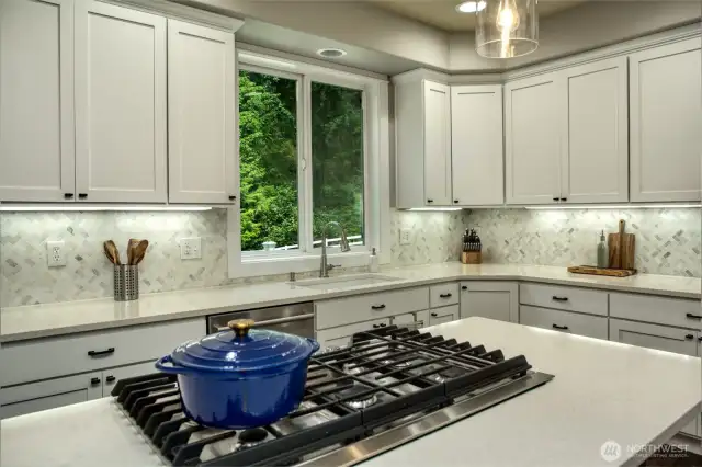 This pristine kitchen features a sleek gas cooktop on the quartz island, under-cabinet lighting, and expansive counter space offering both elegance and function.