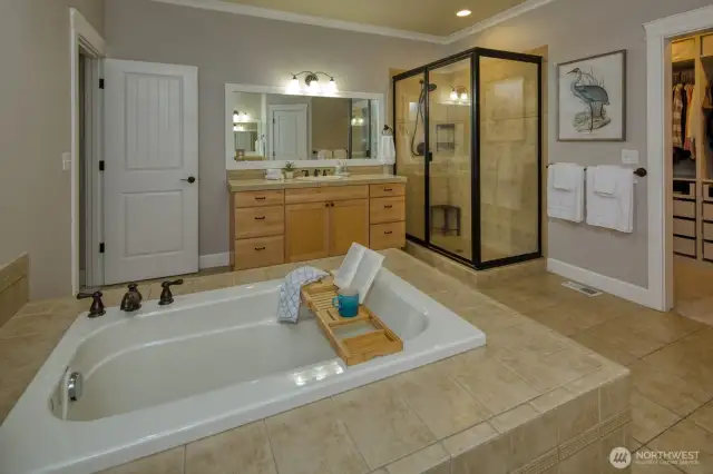This luxurious primary bath offers a spacious walk-in shower, deep soaking tub, and dual-sink vanity with warm wood cabinetry—all complemented by tile flooring and easy access to the custom walk-in closet.