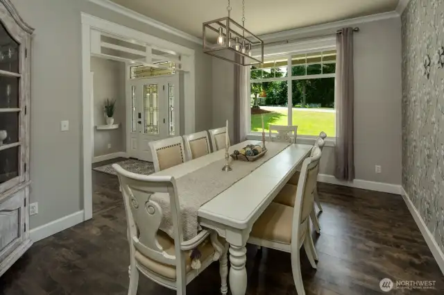 This bright and welcoming dining space opens gracefully to the front entry, showcasing elegant millwork, warm hardwood floors, and a large window that fills the room with natural light and picturesque garden views.