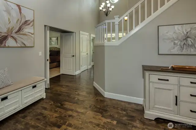 This elegant entry hall welcomes you with soaring ceilings, rich hardwood floors, and stylish lighting, leading to the main floor primary suite and the main staircase adds architectural charm to this beautifully designed home.