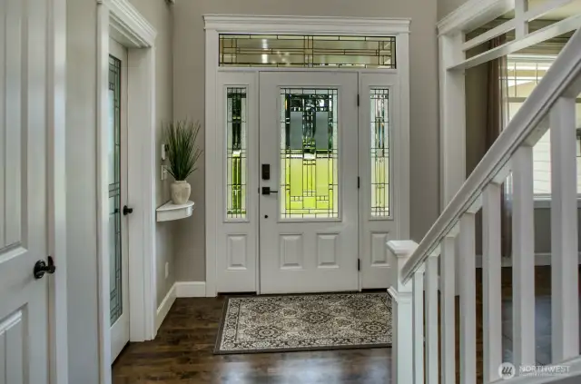 Step inside to a sunlit foyer with rich hardwood flooring, crisp white millwork, and a beautifully crafted glass entry door that floods the space with natural light.