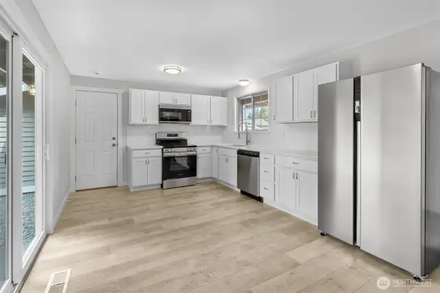 Brand new white plywood cabinetry and Frigidaire stainless appliances in the Kitchen. Slider opens to yard while doorway leads to attached garage.