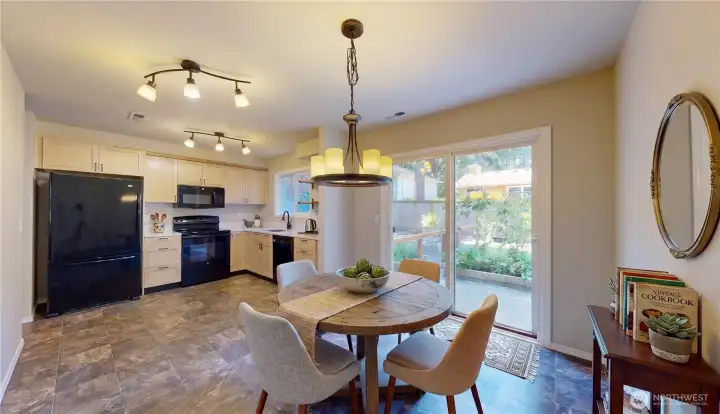 Open kitchen and dining area featuring light wood cabinetry, modern lighting, and sliding doors to the backyard. This photo is virtually staged.