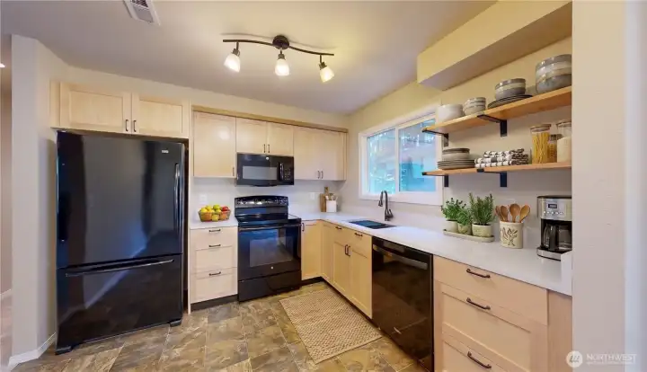 Updated kitchen featuring light wood cabinetry, sleek black appliances, crisp white countertops, and modern open shelving. This photo is virtually staged.