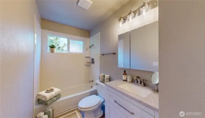 Updated full bathroom featuring a vanity, countertops, clear-glass vanity lighting, and a tub/shower combo. This photo is virtually staged.