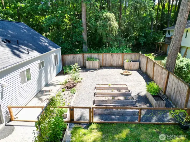 Backyard featuring a premium garden setup with tiered raised beds, custom planters, a built-in fire pit, and a beautiful, private treed backdrop!