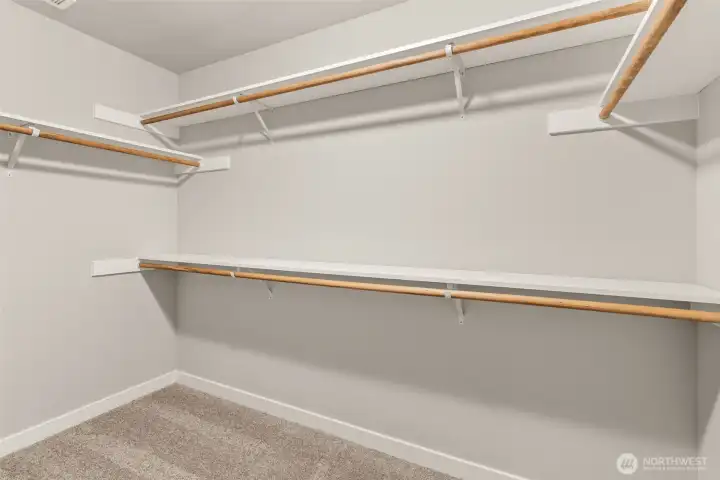 Primary walk-in closet features wood shelves and rods