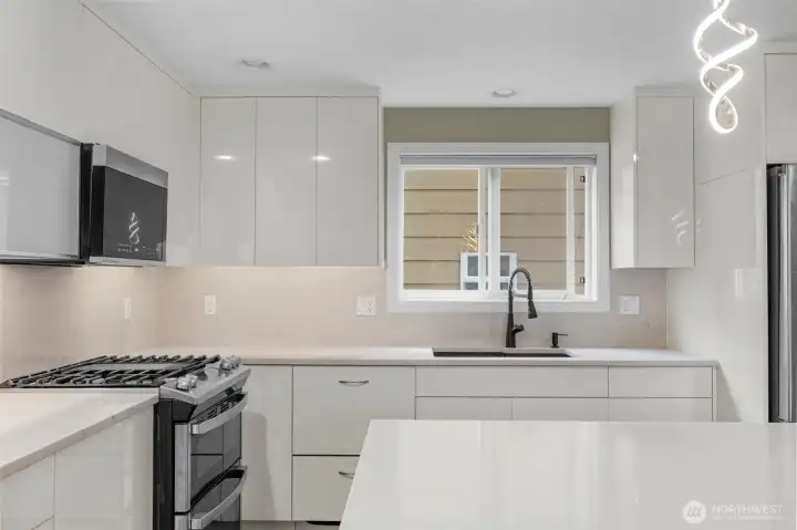 A gourmet chef’s kitchen features custom white cabinetry with sleek push-to-open design, creating a clean, modern aesthetic free of visible hardware. Paired with stainless steel appliances, the space feels effortlessly refined, blending minimalist style with high-end functionality.