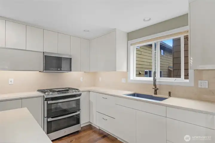 A gourmet chef’s kitchen features custom white cabinetry with sleek push-to-open design, creating a clean, modern aesthetic free of visible hardware. Paired with stainless steel appliances, the space feels effortlessly refined, blending minimalist style with high-end functionality.