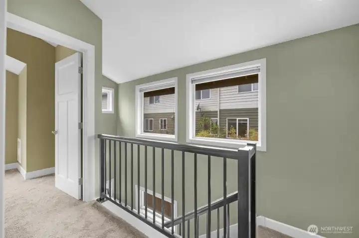 The top-floor hallway offers a clean, modern design featuring a convenient stacked washer and dryer for everyday ease. Sleek metal railings add a contemporary touch while enhancing the open feel and flow of the upper level.